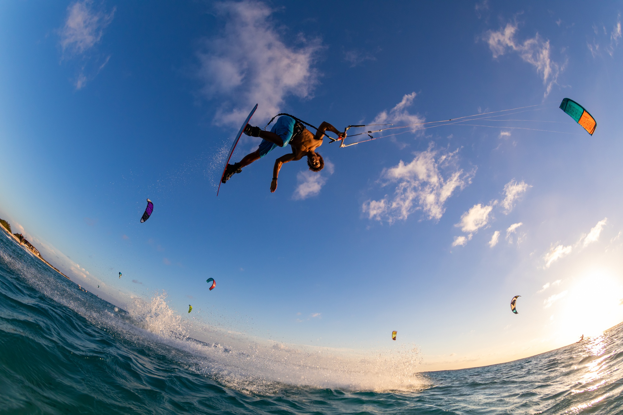 A kitesurfer defies gravity with an aerial trick over crystal-clear waters at sunset. Embrace the adventure with Edge Defiers' extreme sports apparel.